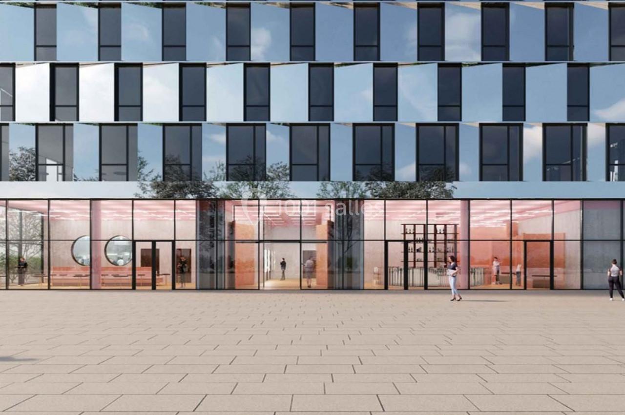 Façade moderne d'un bâtiment avec de grandes baies vitrées, reflétant le ciel et entourée d'une place pavée.