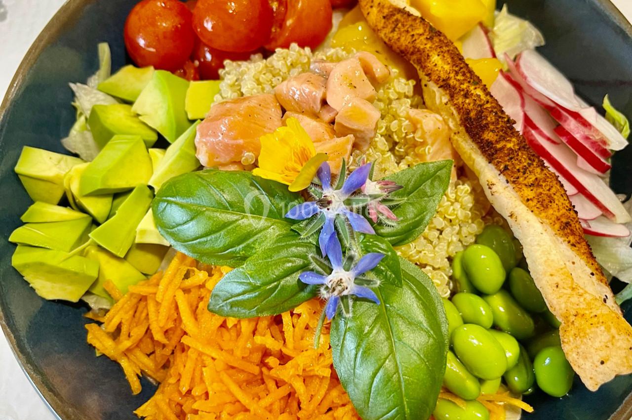 Bol coloré avec quinoa, avocat, tomates cerises, saumon, edamame, carottes râpées, radis et herbes fraîches.