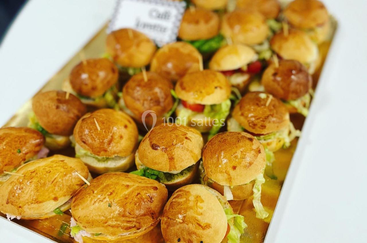 Plateau de mini-burgers garnis de salade, fromage et légumes, présentés sur un support doré.