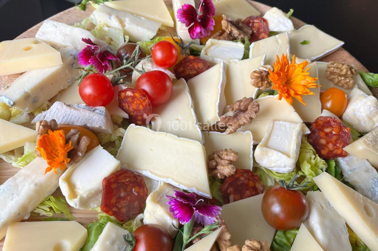 Plateau de fromages variés avec noix, tomates cerises, tranches de chorizo et fleurs comestibles sur un lit de salade.