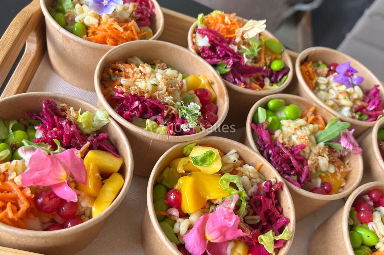 Assortiment de salades colorées dans des bols en carton, garnies de légumes, fruits et fleurs comestibles.