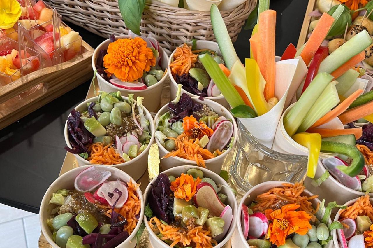 Coupes individuelles de crudités colorées avec carottes, radis, edamame et fleurs comestibles, accompagnées de bâtonnets de…