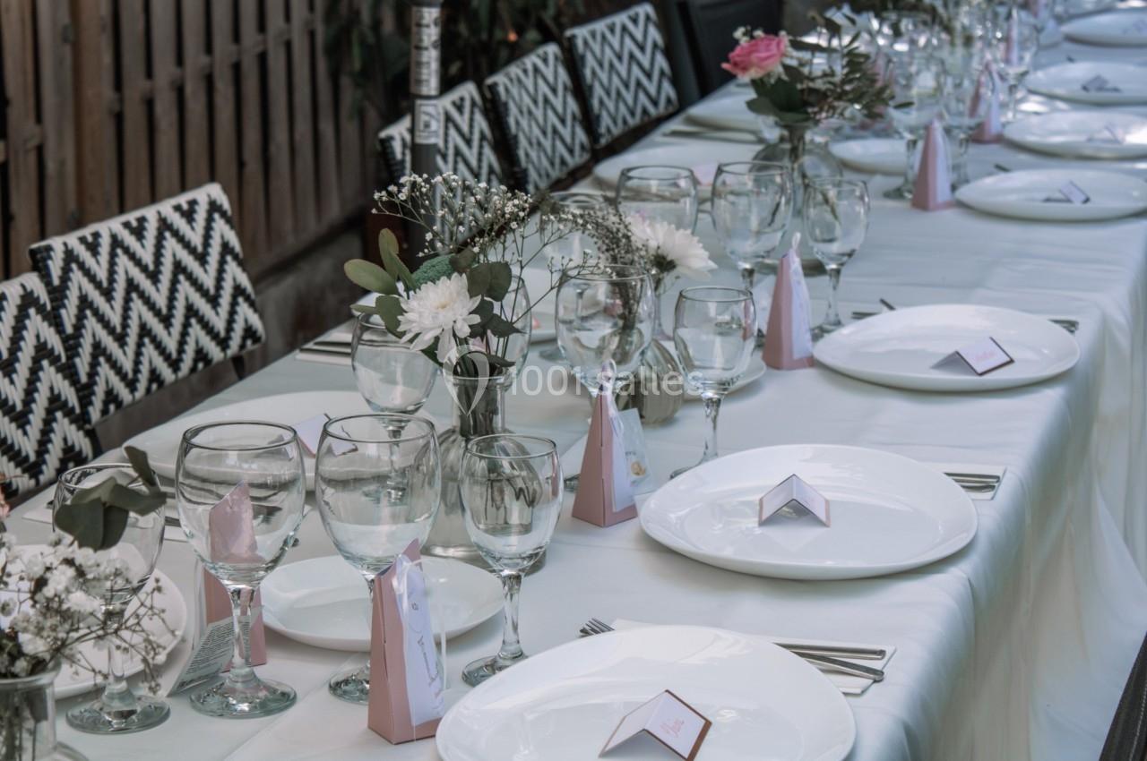 Table dressée avec nappes blanches, assiettes, verres, couverts et décorations florales pour un repas formel.