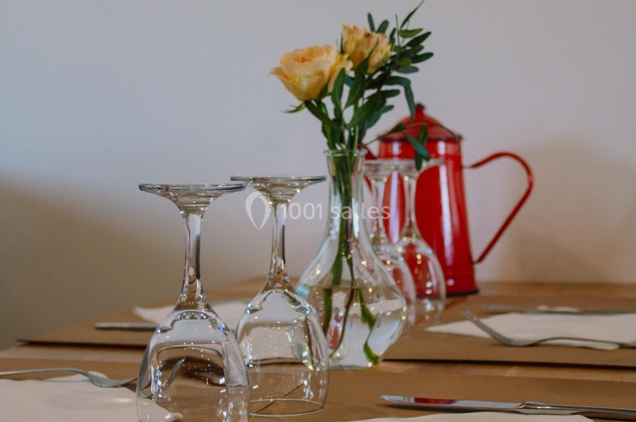 Table dressée avec des verres retournés, des serviettes blanches, un vase contenant des fleurs jaunes et une cafetière rouge.