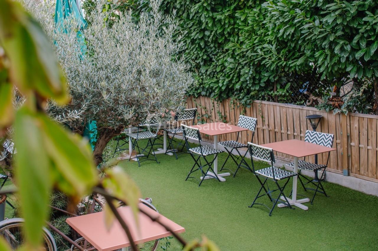 Terrasse extérieure avec tables et chaises sur gazon synthétique, entourée de végétation et d'une clôture en bois.