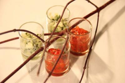 Quatre verrines contenant des préparations colorées, rouges et vertes, décorées de branches fines sur une table blanche.