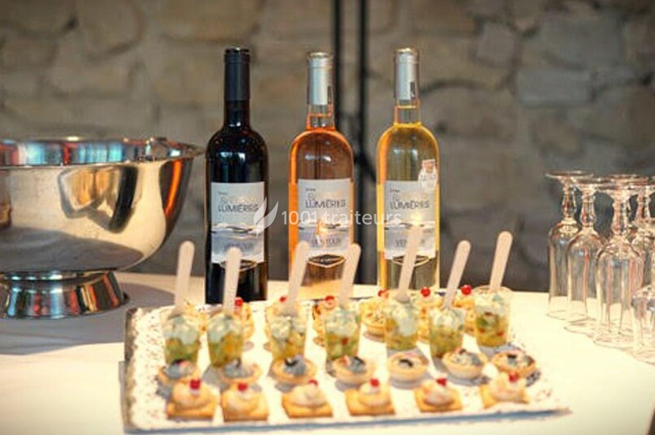 Plateau de verrines et amuse-bouches devant trois bouteilles de vin rouge, rosé et blanc, avec des verres à pied à côté.