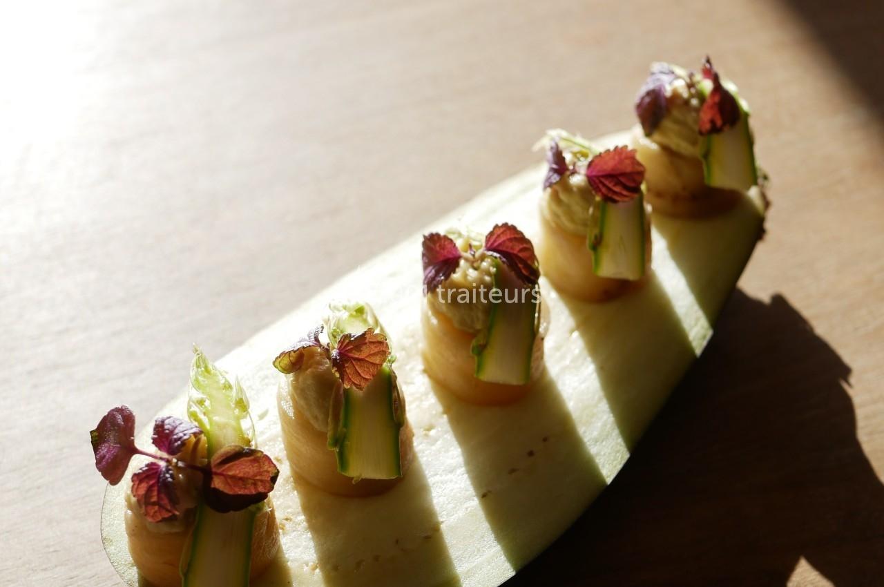 Tranche de courgette garnie de purée et décorée de petites feuilles et légumes, posée sur une table en bois.