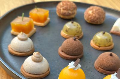 Assortiment de mini-pâtisseries variées disposées sur une assiette noire, présentées sur une table en bois.
