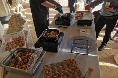 Chef cuisinant des plats à base de crevettes et œufs devant une table dressée en extérieur.