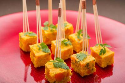 Bouchées apéritives carrées surmontées de feuilles de persil, présentées avec des piques en bois sur une assiette rouge.