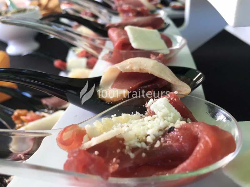 Tranches de viande crue servies sur des cuillères avec des copeaux de fromage et une présentation soignée.