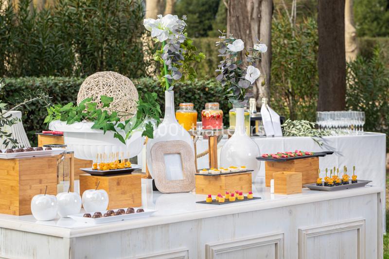 Table de buffet en extérieur avec décorations florales, verrerie, boissons et assortiments de bouchées apéritives.