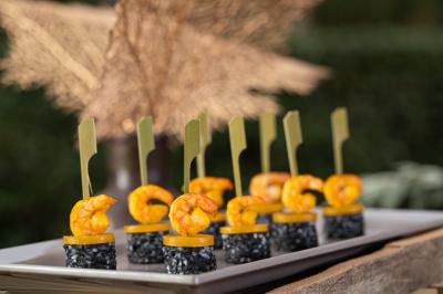 Brochettes de crevettes grillées sur morceaux de riz noir enrobé de sésame, présentées sur un plateau.