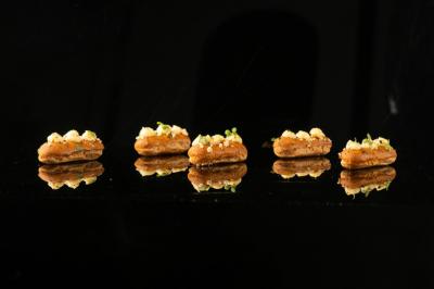 Quatre amuse-bouches disposés en ligne sur une surface noire réfléchissante, garnis de crème et de fines herbes.