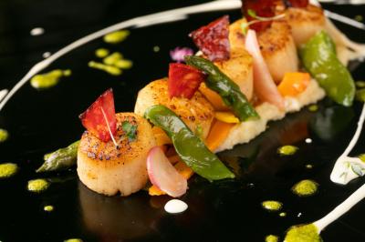 Noix de Saint-Jacques poêlées servies avec légumes colorés, purée et décorations culinaires sur une assiette noire.