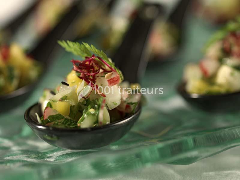 Petites cuillères noires garnies de dés de légumes colorés et herbes fraîches, disposées sur une nappe verte.