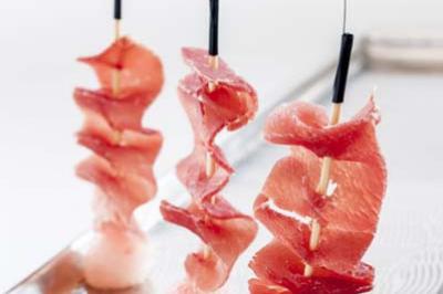 Tranches fines de jambon enroulées sur des brochettes, présentées verticalement sur des supports sphériques.