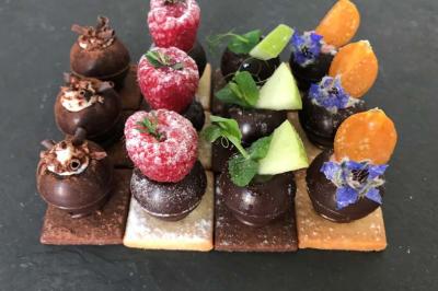 Assortiment de petits desserts sur biscuits, décorés de fruits frais, fleurs comestibles et copeaux de chocolat.