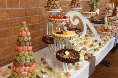 Table garnie de desserts variés, incluant des pyramides de macarons, gâteaux et verrines, dans une salle au mur en briques.