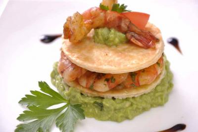 Millefeuille salé composé de crevettes, guacamole et galettes croustillantes, décoré de persil et tomate.