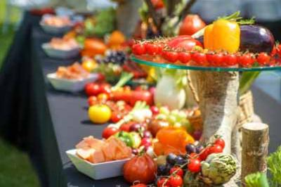 Table garnie de légumes et fruits colorés disposés sur des présentoirs en extérieur.