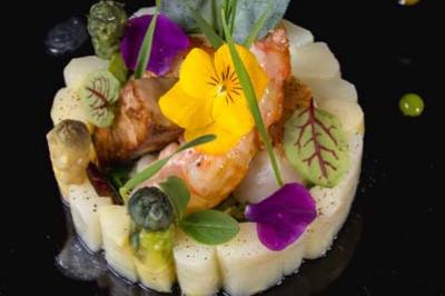 Assiette gastronomique avec purée dressée en cercle, asperges, crevettes, fleurs comestibles et sauce décorative.