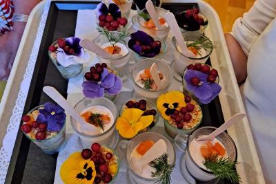 Plateau de verrines décorées de fleurs comestibles, baies rouges et herbes fraîches, présenté sur un fond clair.