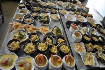 Plateaux garnis de petites portions variées, incluant fruits de mer, légumes et sauces, disposés sur une table en cuisine.