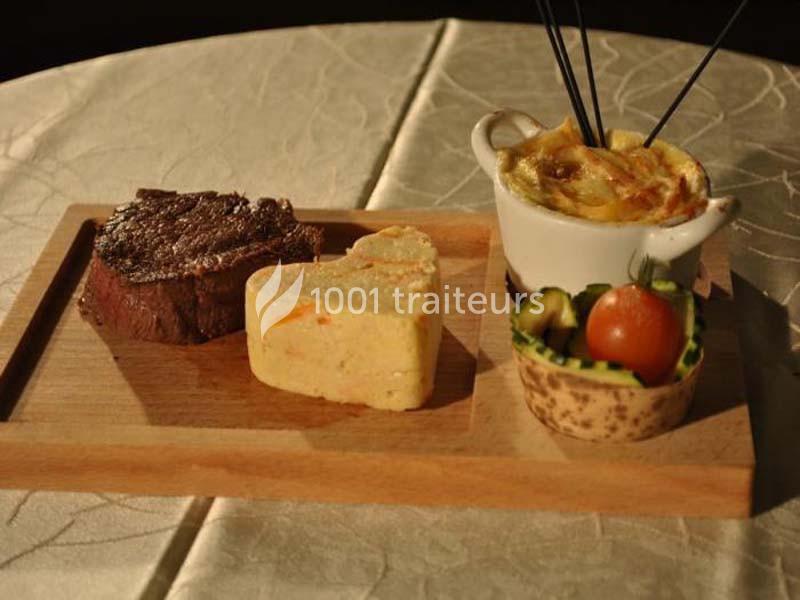Assiette en bois avec un steak, un gratin en ramequin, une purée en forme de cœur et une garniture de légumes.