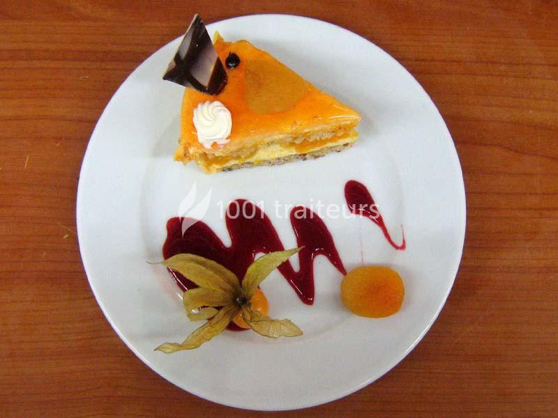 Part de gâteau à l'orange décorée de chocolat, crème et physalis, accompagnée de coulis rouge sur une assiette blanche.