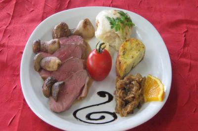 Assiette composée de tranches de viande, champignons, tomate, gratin, confit d'oignons, sauce décorative et tranche d'orange.