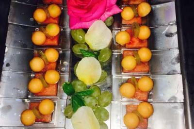 Plateau décoratif avec des morceaux de melon, raisins, cubes de pastèque et une rose rose au centre.