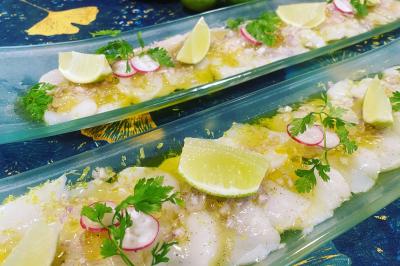 Tranches de poisson cru marinées, garnies de citron, radis, herbes fraîches et servies sur des plats en verre.