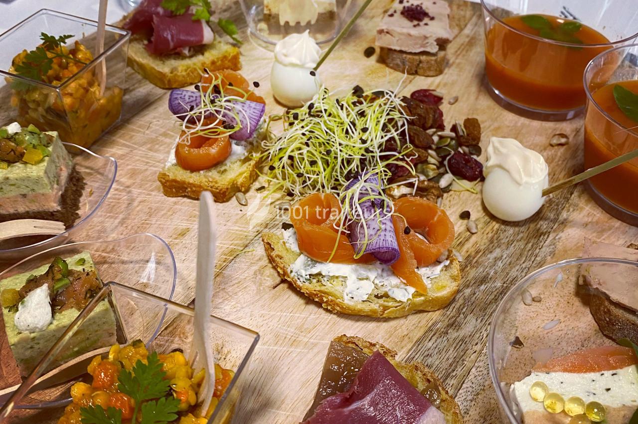 Plateau en bois garni d'amuse-bouches variés, incluant saumon fumé, tartares, verrines et décorations végétales.