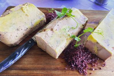 Bloc de foie gras tranché sur une planche en bois, accompagné de sel noir et décoré de pousses vertes.