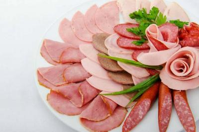 Assortiment de charcuteries variées disposées sur une assiette blanche, décorée de persil et d'oignons verts.