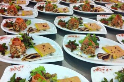 Plats dressés sur des assiettes blanches avec terrines, légumes et garnitures, alignés dans une cuisine professionnelle.