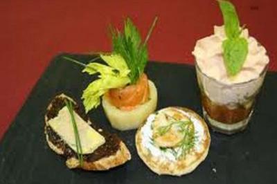 Assortiment de bouchées apéritives comprenant toast, blini, roulé de saumon et verrine sur ardoise noire.