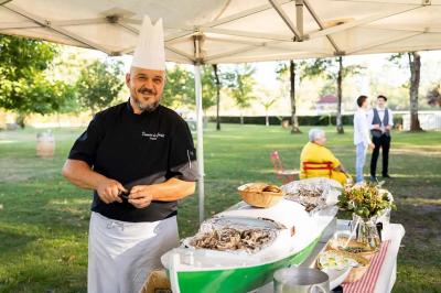 Un chef en tenue prépare des huîtres sous une tente dans un cadre extérieur verdoyant avec des invités en arrière-plan.