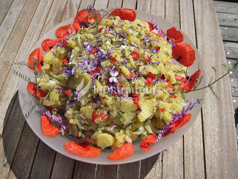 Salade de pommes de terre garnie de fleurs comestibles colorées, présentée dans un plat sur une table en bois.