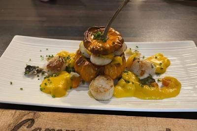 Assiette gastronomique composée de noix de Saint-Jacques, sauce jaune et légumes, présentée sur une assiette blanche.