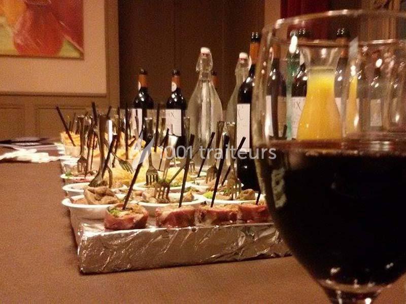 Verres de vin et buffet composé de plats variés, bouteilles et carafes disposés sur une table dans une salle.