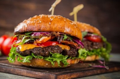 Deux hamburgers garnis de salade, tomates, oignons rouges, fromage fondu et bacon, servis sur une planche en bois.