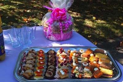 Plateau de petits fours variés sur une table violette en extérieur, avec un panier cadeau en arrière-plan.