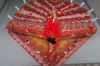 Plateau de charcuterie en forme de paon, décoré de tranches de viande, olives, tomates et rubans rouges.