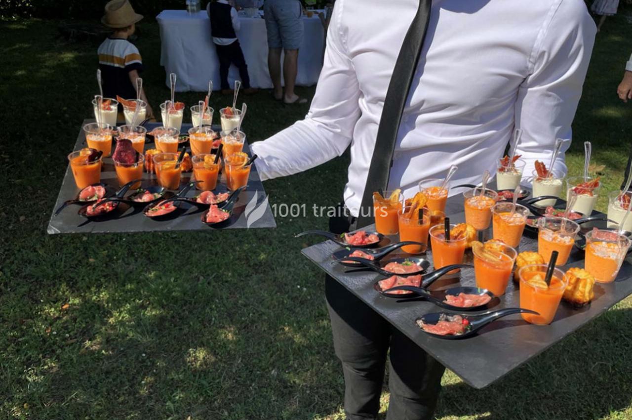 Serveur tenant deux plateaux garnis de verrines et amuse-bouches lors d'un événement en extérieur.