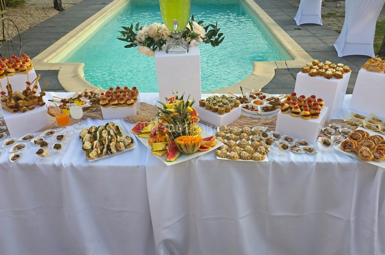 Buffet de desserts variés et colorés disposés sur une table blanche près d'une piscine extérieure.