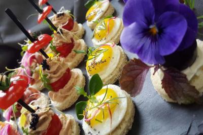 Assortiment de canapés garnis de légumes, œufs, herbes fraîches et fleurs comestibles sur un plateau sombre.