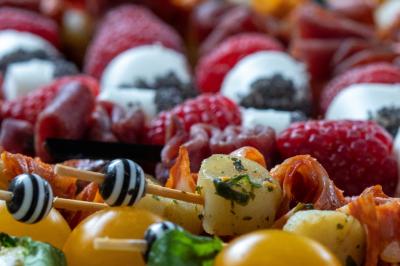 Plateau coloré de brochettes apéritives avec tomates cerises, mozzarella, crevettes, framboises et charcuterie.